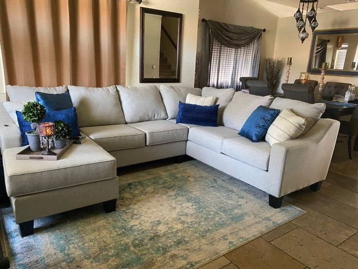 A Living Room With A Large Sectional Couch And Blue Pillows On The Back ... in